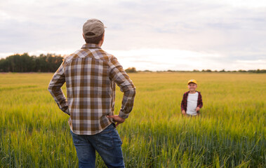 Farmer and his son in front of a sunset agricultural landscape. Man and a boy in a countryside field. Fatherhood, country life, farming and country lifestyle concept.