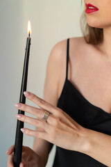 A young woman with red lipstick in a black dress holds a burning candle.