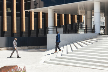 Greeting and handshake of two afro american businessmen partner against the backdrop of a modern building exterior. Friendly meeting outdoors