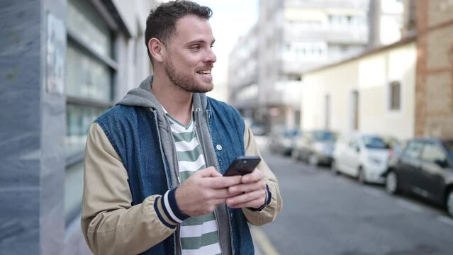 Young caucasian man smiling using smartphone at street