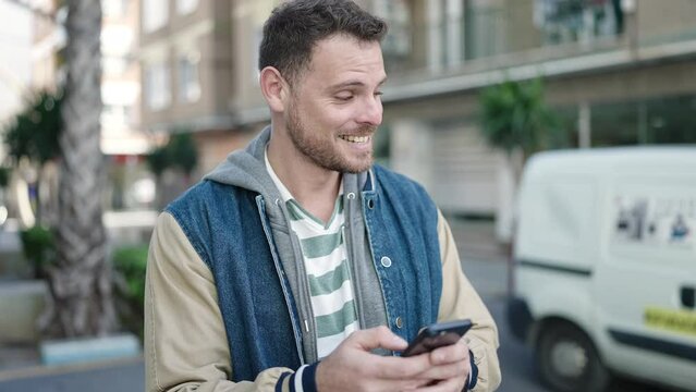 Young caucasian man smiling using smartphone at street