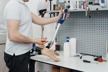 Crop unrecognizable craftsman adjusting and bending modern prosthetic leg at knee section at workbench in manufacturing factory