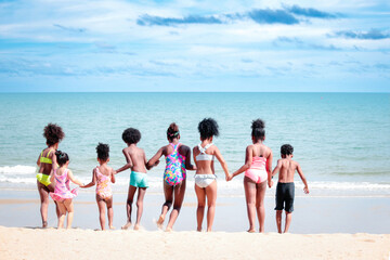 Group of African kids in swimsuit from behind have fun together on summer beach, boys and girls...