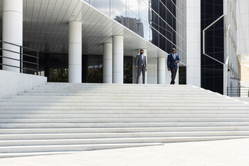 Business people walk down the stairs to a modern glass building. Work in a large company. Career growth and advancement. Increasing and improving skills. Salary increase