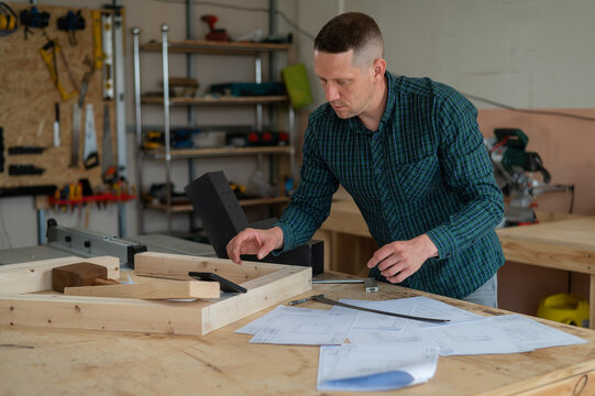 Portrait of a carpenter in a plaid shirt working on a plan in a workshop. 