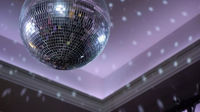 Silver mirror disco ball suspended from the ceiling rotates quickly, light spot rays and glare. White stage light at a concert hall, club, party or disco. Illumination and atmosphere.