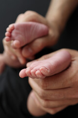 A mother hold the feet of a newborn child in a black blanket on a Black background. The feet of a newborn in the hands of parents. Studio macro photo legs, toes, feet and heels of a newborn.