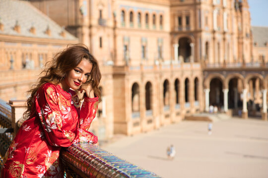 A beautiful young woman wearing a traditional Moroccan red dress with gold and silver embroidery is on vacation in Seville, Spain.