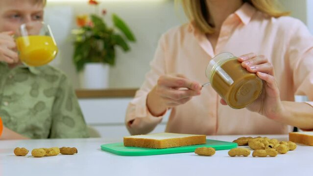 Mother preparing sandwitch with peanut butter while son eating it