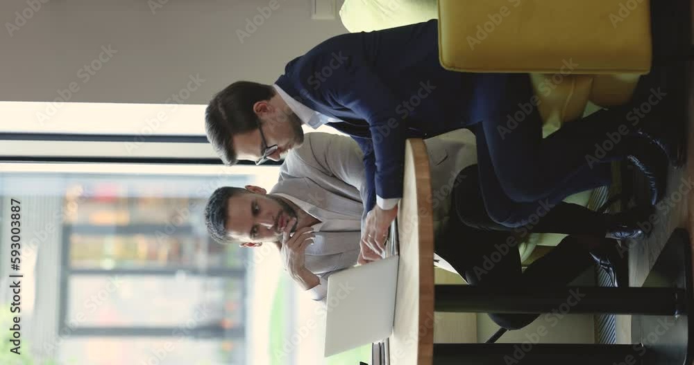 Poster two businessmen meeting at laptop in office lounge cafe, discussing online video content, project pr