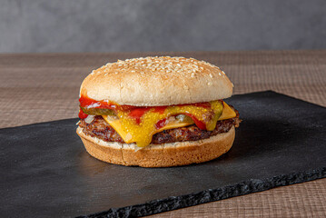 beef burger, cheese, onion, ketchup, mustard , on black isolated plate resting on wooden table horizontal photo in natural light