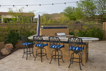 A desert landscaped backyard in Arizona featuring a travertine tiled pool deck, spa and outdoor kitchen.
