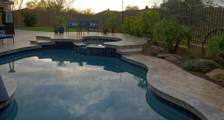 A desert landscaped backyard in Arizona featuring a travertine tiled pool deck, spa and outdoor kitchen.