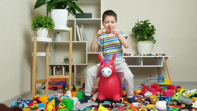 A little boy is jumping on an inflatable rubber donkey among the mess in the children's room. Bouncing toy for kids.