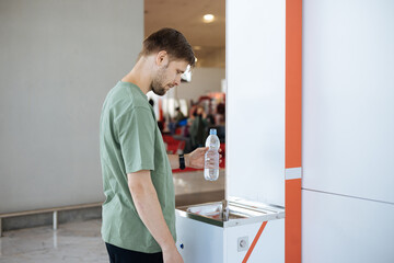 Man refilling his plastic bottle at the airport water fountain. Free public water bottle refill station. Sustainable and green life. Tap refill to reduce plastic bottle usage. Drinking water dispenser