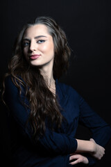 Fototapeta premium Make-up and fashion concept. Brunette woman with long wavy hair sensual studio portrait. Model wearing blue blouse and looking at camera with blue eyes and seductive look. Toned image with blue color