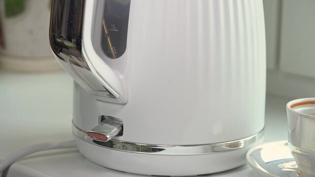 White electric kettle boils water. Turning on the kettle to make tea or coffee in the morning