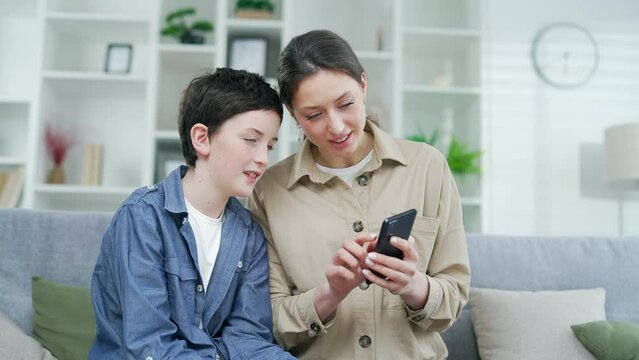 Mother with a child, a teenage son, use a smartphone with a mobile phone making food delivery order, buying on e-commerce websites, watch cartoons, have fun on weekend use internet modern tech concept