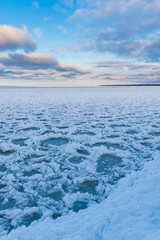 A serene winter landscape of an icy lake in Sweden, surrounded by blue skies and snow-covered clouds. Tranquility reigns with no people or wind waves disrupting the frozen beauty.