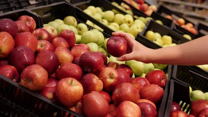 Close-up of a woman choosing red apples in a supermarket. A woman's hand with a red apple in a grocery store. 
