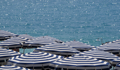 Parasols blancs et bleus et mer bleue sur une plage privée. Côte d'azur, France - obrazy, fototapety, plakaty