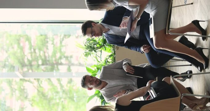 Group of positive businesspeople talking, chatting on corporate meeting, sitting on chairs in circle, enjoying teambuilding briefing speaking, smiling, giving support, help, advice to colleague