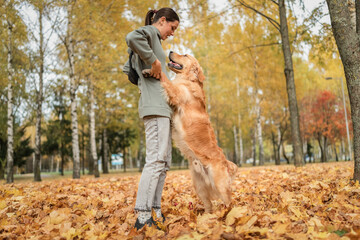 A beautiful young dark-haired girl plays in the autumn park with a golden retriever.