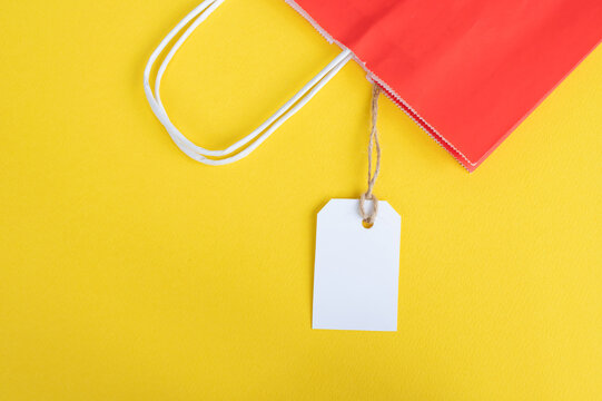 White tag with a paper red bag for recycling on a yellow background. paper bag handles