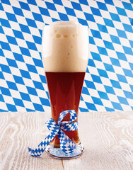 Dark wheat beer in glass on Bavarian pattern background