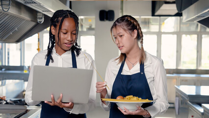 Two African and Asian students stand in a cooking class. on campus learning to cook Discuss food...