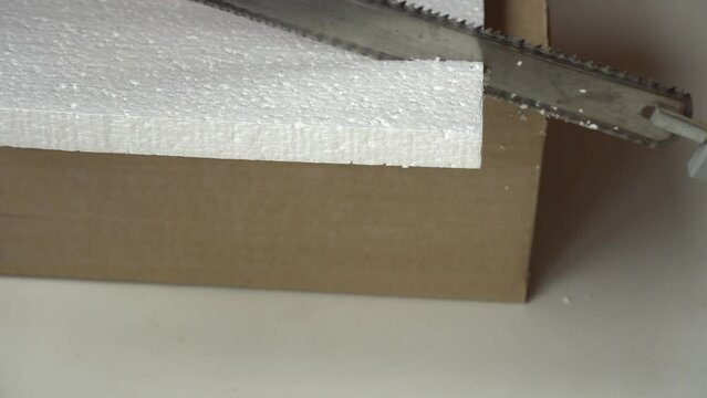 The hacksaw cuts Styrofoam. Cutting process of white Styrofoam