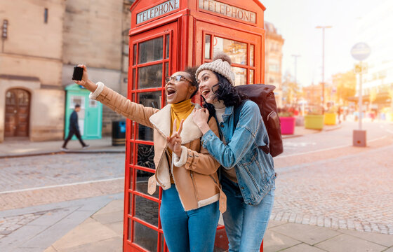two friend, girlfriend and women using a mobile phone, camera and taking selfie against a red phonebox in the city of England.Travel Lifestyle concept