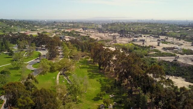 descending aerial footage over the rippling waters of a lake with lush green trees and grass and people walking along a path, blue sky and clouds at Kenneth Hahn State Recreation Area in Los Angeles
