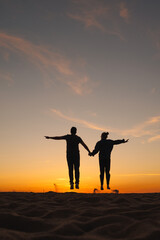Fototapeta na wymiar couple of man and woman holding hands jumping on background of the sky. sunset walk on seashore, nature background. joke and fun, relationships and carefree communication