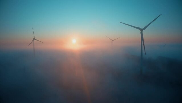 Wind farm at sunrise in heavy fog. Wind turbines generating green energy - concept of renewable electricity, sustainable energy, green power production
