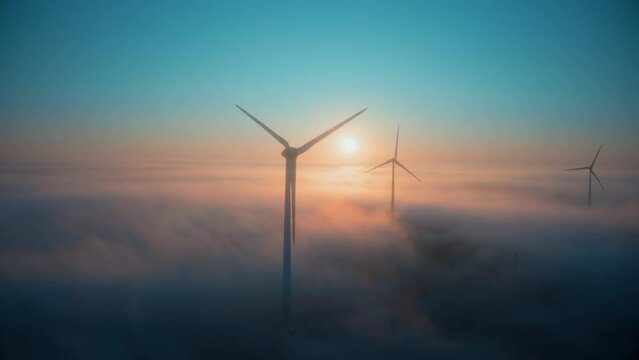 Wind farm at sunrise in heavy fog. Wind turbines generating green energy - concept of renewable electricity, sustainable energy, green power production