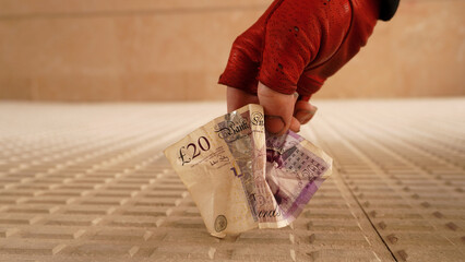 a hand in a red glove lifts twenty pounds sterling from the ground