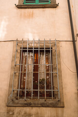 Antique old window with black iron bars framed on a light yellow wall. Pisa, Italy