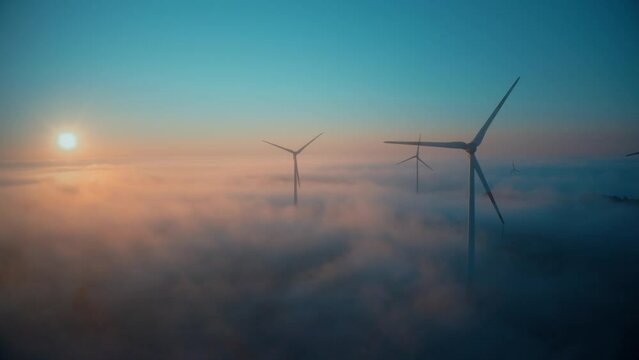 Wind farm at sunrise in heavy fog. Wind turbines generating green energy - concept of renewable electricity, sustainable energy, green power production