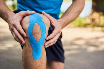 Close-up of male runner holding injured knee with kinesiology tape. Kinesiotaping concept - obrazy, fototapety, plakaty
