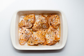 Raw marinated chicken legs in ceramic cooking tray. On white background