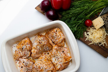 Raw marinated chicken legs in ceramic cooking tray. Fresh vegetables on cutting board