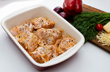 Raw marinated chicken legs in ceramic cooking tray. Fresh vegetables on cutting board