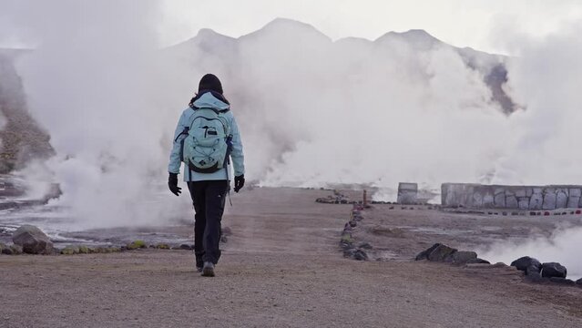 Adventurous woman walking towards water steam in slow motion at El Tatio Geyser Field. Third-largest geyser field in the world.