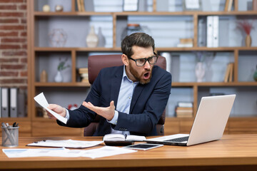 Obraz premium Angry shouting boss talking on video call with colleagues subordinates, man showing laptop document unsatisfactory report to camera, businessman mature adult in business suit working inside office.