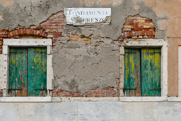 Detail of the facade of an old house with a pair of closed windows under the weathered sign of...