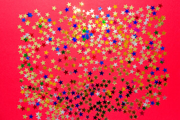 Multi-colored shining stars close-up. Festive holiday background. Stars on a red paper background.	
