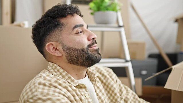 Young hispanic man sitting on floor breathing at new home