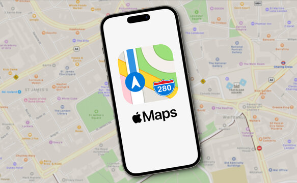 Apple Maps logo with lettering is displayed on a smartphone lying on a map view of Apple Maps