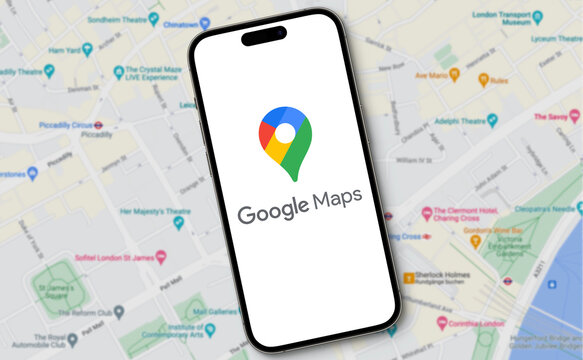 Google Maps logo with lettering is displayed on a smartphone lying on a map view of Google Maps